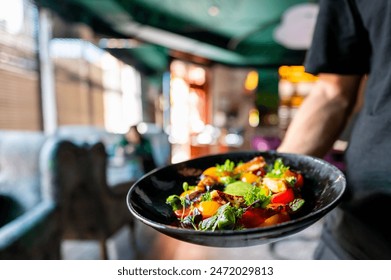 Close-up of a colorful salad on a black plate, being served in a restaurant setting - Powered by Shutterstock