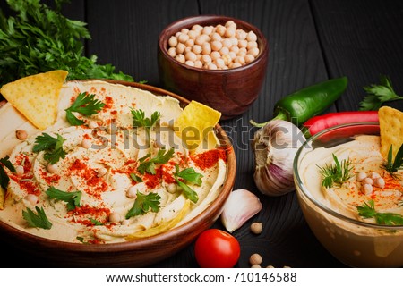 A close-up of a colorful snack composition on a black wooden background. Delicious hummus in glass bowl and on a wooden plate. Stok fotoğraf © 