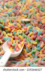 Closeup Of Colorful Sour Worms Candy Sweets In Transparent Box With White Scoop. Low Sugar Fruit Gummies, Hues Come From Fruit And Veggie Juices. Smart Healthy Living. Vertical Plane.