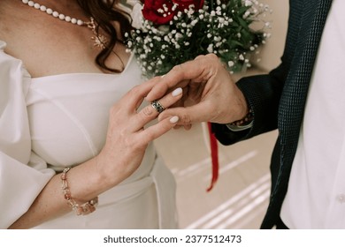 A close-up, colorful wedding photograph capturing the poignant moment when the groom gently places the wedding ring on the bride's finger, symbolizing their love and commitment.