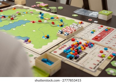 Close-up of a complex strategy board game with hexagonal tiles, colorful wooden cubes, and game pieces on a table, showcasing tabletop gaming hobby, logic, and planning during a social gathering.