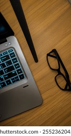 A close-up composition featuring a modern laptop with a glowing blue backlit keyboard on a warm wooden desk.