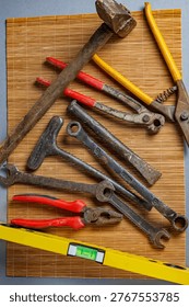 Close-up composition of vintage rusty tools including hammer and wrenches on bamboo mat. Detailed view of worn metal surfaces and construction equipment.