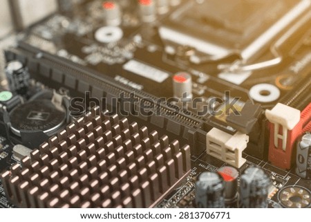 Close-up of a computer motherboard with electronic components, focusing on the heatsink, RAM slots, and capacitors with a warm light flare.