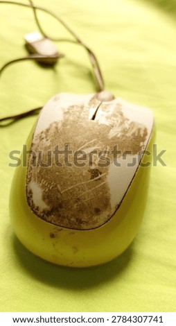 Close-up of a computer mouse with visible dirt stains attached on top of green fabric background. Concept of daily technology use, hygiene, workspace equipment, and realistic object detail suitable for microstock photography. Captured with natural lighting and detailed texture composition
