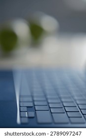 Close-up computer on a table. A new modern blue Apple Neo computer on a table. In the blurred background, light gray tones and a textured wall. Keyboard close-up. Window light. A plate with green apples on the table.