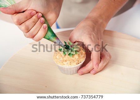 A close-up of a confectioner woman decorates using a pastry syringe and a cap made from natural products with a sweet cream of green color. Dietary Vegan Creamcakes
