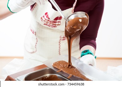 Close-up of a confectioner woman in a white apron pours hot chocolate in a plastic mold to create a chocolate sculpture on a white background - Powered by Shutterstock