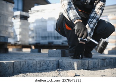 Close-up of construction worker installing and laying pavement stones on terrace, road or sidewalk. Worker using stones and rubber hammer to build stone sidewalk.