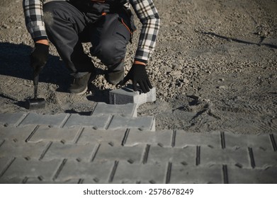 Close-up of construction worker installing and laying pavement stones on terrace, road or sidewalk. Worker using stones and rubber hammer to build stone sidewalk.