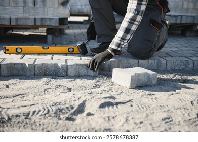 Close-up of construction worker installing and laying pavement stones on terrace, road or sidewalk. Worker using stones and rubber hammer to build stone sidewalk.