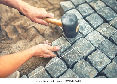 Close-up of construction worker installing and laying pavement stones on terrace, road or sidewalk. Worker using stones and rubber hammer to build stone sidewalk