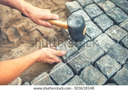 Close-up of construction worker installing and laying pavement stones on terrace, road or sidewalk. Worker using stones and rubber hammer to build stone sidewalk