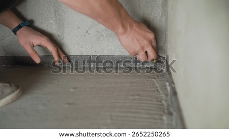 Close-up of a construction worker meticulously applying waterproofing tape to the corner of a bathroom floor, ensuring protection against moisture damage during renovation