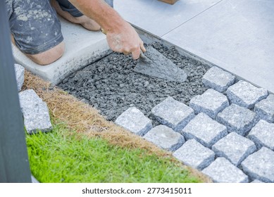 Close-up of a construction worker using a trowel while installing cobblestone pavement on a prepared base, showing landscaping and masonry work in progress.