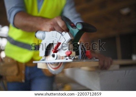 Close-up of construction worker working with eletric saw inside wooden construction of house, diy eco-friendly homes concept.