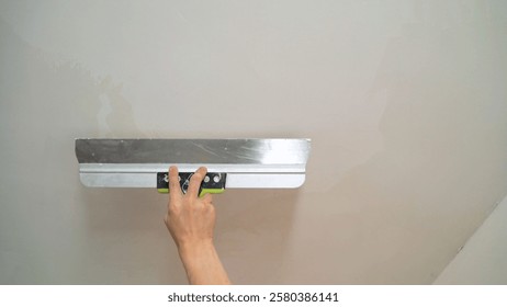 Close-up of a construction worker's hand using a spatula to apply plaster on a wall during renovation or construction work
