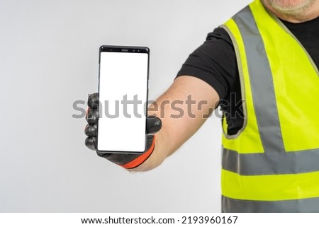 Close-up constructor with vest and gloves presenting cellphone with empty display and copy space area. Construction, architecture, repair work. Calling the master by phone. Mobile app for repairmen.