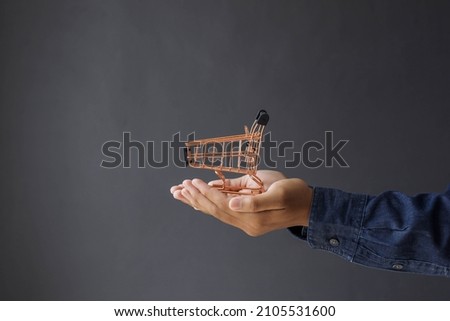 Close-up of consumer's hand giving mini shopping cart isolated on gray background