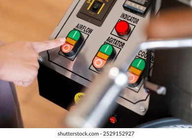 A close-up of a control panel featuring buttons labeled airflow, agitator, and cooler. A finger is pressing the airflow button. The panel has various indicators a