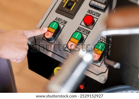 A close-up of a control panel featuring buttons labeled airflow, agitator, and cooler. A finger is pressing the airflow button. The panel has various indicators a