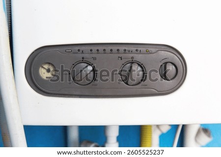 Close-up of control panel of gas boiler with dials and pressure gauge, showing heating settings and temperature indicators in domestic environment