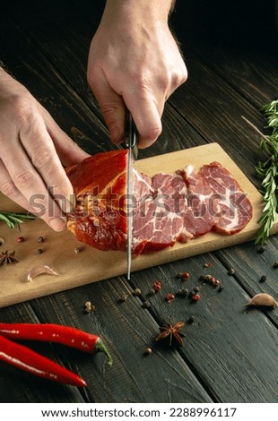 Close-up of a cook hands with a knife cut ham into thin slices for a sandwich. Fast food concept on dark background