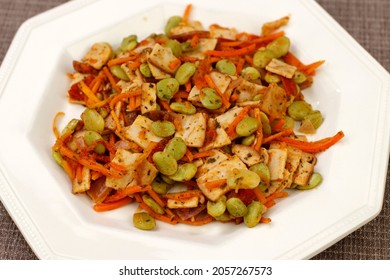 Close-up Of Cooked Meal Of Organic Turkey, Carrots, Lima Beans, Tomato, Onions And Parsley Served On A Plate. Meal Of Organic Turkey With A Few Vegetables On An Octagon White Plate On A Brown Placemat