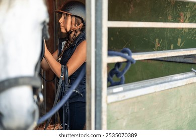 closeup copyspace young female rider, wearing a helmet, carefully prepares her horse in the stable for a riding session at the equestrian center. She adjusts the saddle and checks the bridle - Powered by Shutterstock