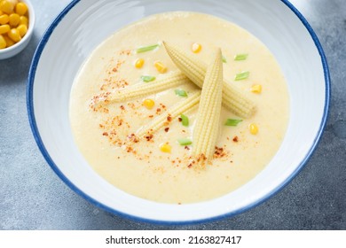 Close-up of corn cream-soup with addition of baby corncobs served in a white plate, selective focus