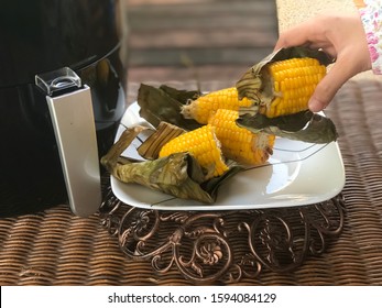 Closeup Corn Roasted With Air Fryer In The White Plate On The Rattan Table.Women’hand Taking.Ready To Eat.Outdoor,balcony,garden.