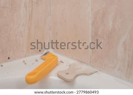 Closeup of corner scraper and plastic spatula for removing seams. Tools for tile repair and restoration on bathtub edge