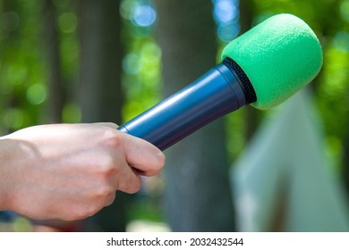 Close-up Of A Correspondent's Hand Holding A Microphone With A Green Foam Nozzle From The Wind