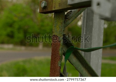 Close-up of a corroded metal gate post showing rust and flaking green paint. The image captures textured decay on the vertical pole, a corroded bracket
