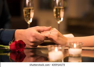 Closeup of couple hands on restaurant table with two glasses of champagne. Romantic couple holding each other's hand at dinner in a luxury restaurant. Marriage proposal and engagement concept.

