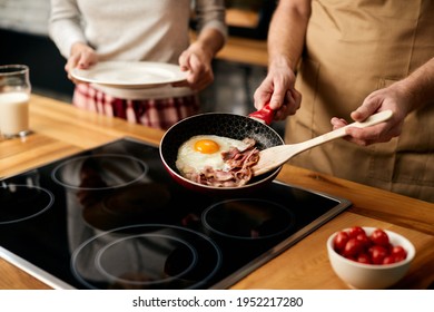 Close-up Of Couple Having Breakfast At Home. Man Is Preparing Eggs And Bacon In Frying Pan. 