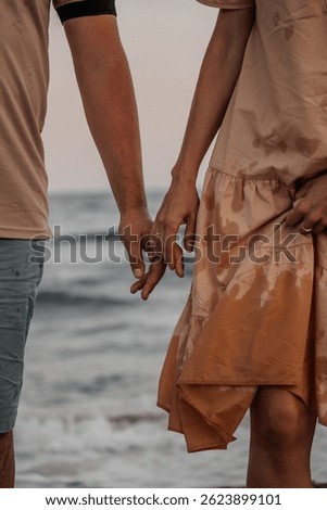 A close-up of a couple holding hands while walking by the sea. Their intertwined fingers symbolize love, trust, and connection, captured in a romantic seaside setting.