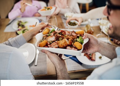 Close-up Of Couple Passing Food To Each Other While Having Lunch With Their Family. 