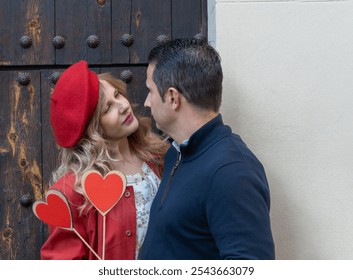 A close-up of a couple as they exchange a loving look, holding sticks with heart cutouts, complemented by a rustic door backdrop - Powered by Shutterstock