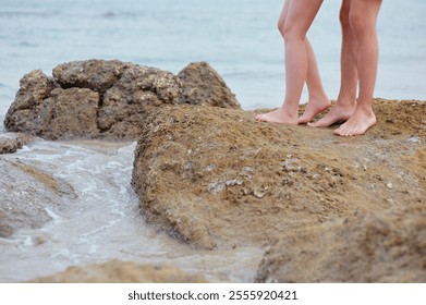 A close-up of a couple's bare feet on seaside rocks, capturing a moment of intimacy and romance. Waves gently crash against the shore, enhancing the serene atmosphere. - Powered by Shutterstock