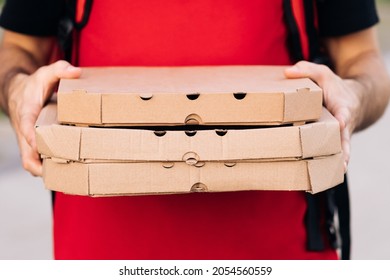 Close-up of the couriers hands and pizza. Portrait of delivery man holding cardboard pizza box against city, courier food delivery. Delivery man holding boxes with hot pizza, food order online - Powered by Shutterstock