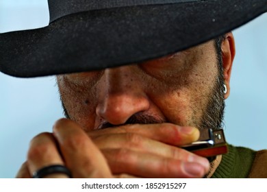 Close-up, a cowboy plays the harmonica in his mouth with his hat covering his eyes. Western spaghetti