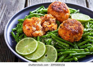 Close-up Of Crab And Prawn Cakes On A Plate With Boiled Green Beans, Lime On A Wood Table, Horizontal View From Above