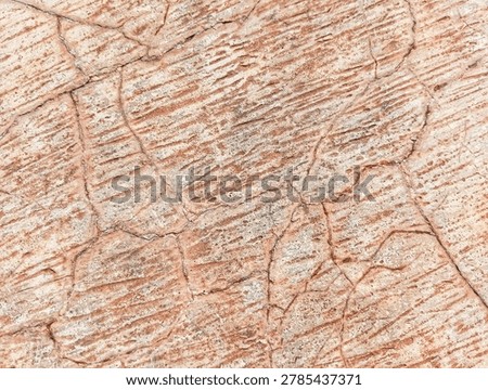 Closeup of cracked stone surface with reddish brown lines and parallel striations. Earthy tones of beige and terracotta creating natural abstract pattern.