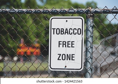 Closeup Of Cracked White Tobacco Free Zone At A School Football Field With Chain Linked Metal Fence