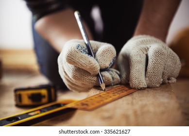 Close-up of craftsman hands in protective gloves measuring wooden plank with ruler and pencil. Woodwork and renovation concept.  - Powered by Shutterstock