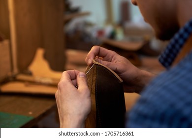 Closeup of craftsman hands sewing brown leather parts with needle for future case for glasses. The man with needle sewing leather in the workshop. The craftsman while sewing leather case for glasses - Powered by Shutterstock