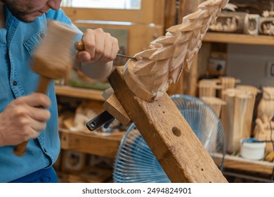 close-up of a craftsman using wood chisel and hammer for carving a Christmas pine tree out of wood. Interior workshop, wood carving, Italy. Traditional equipment.