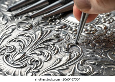 CLOSEUP OF CRAFTSMAN'S HAND EMBOSSING METAL WITH PUNCH IN THE WORKSHOP. GOLDSMITH, SILVERSMITH, JEWELLERY AND HANDICRAFTS CONCEPT.