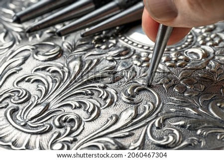 CLOSEUP OF CRAFTSMAN'S HAND EMBOSSING METAL WITH PUNCH IN THE WORKSHOP. GOLDSMITH, SILVERSMITH, JEWELLERY AND HANDICRAFTS CONCEPT. Foto d'archivio © 
